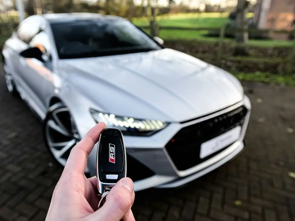 Hand mit Autoschlüssel vor einem neuen Auto